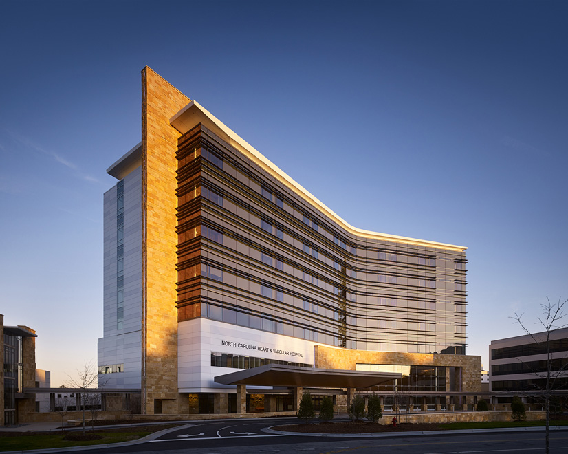 The North Carolina Heart & Vascular Hospital is a tall building of modern architcture, framd by the sunset.